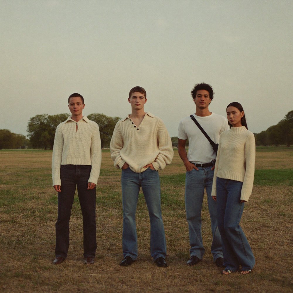 Four people standing in an open park wearing cream knitwear and jeans